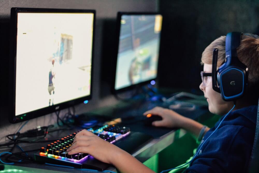 Menino jogando no PC, com acessórios RGB e setup gamer.