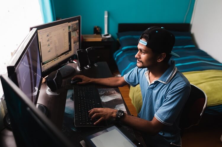 Homem em um quarto mexendo em dois computadores