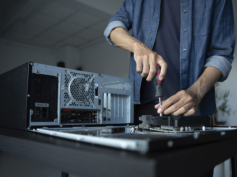 Pessoa montando ou consertando um computador desktop, utilizando ferramenta de chave de fenda, em ambiente interno com foco na ação de manutenção de hardware.