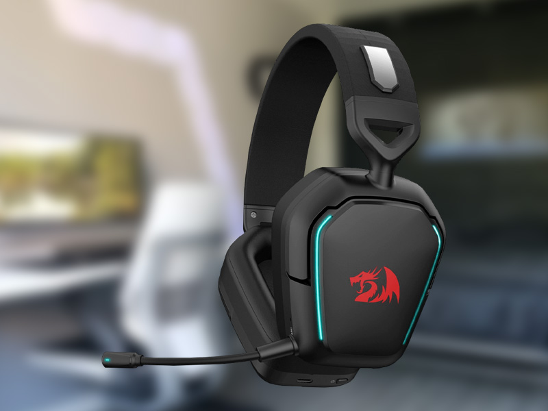 Fone de ouvido gamer com microfone, headset preto com detalhes em azul e logotipo de dragão vermelho em fundo desfocado de ambiente interno.