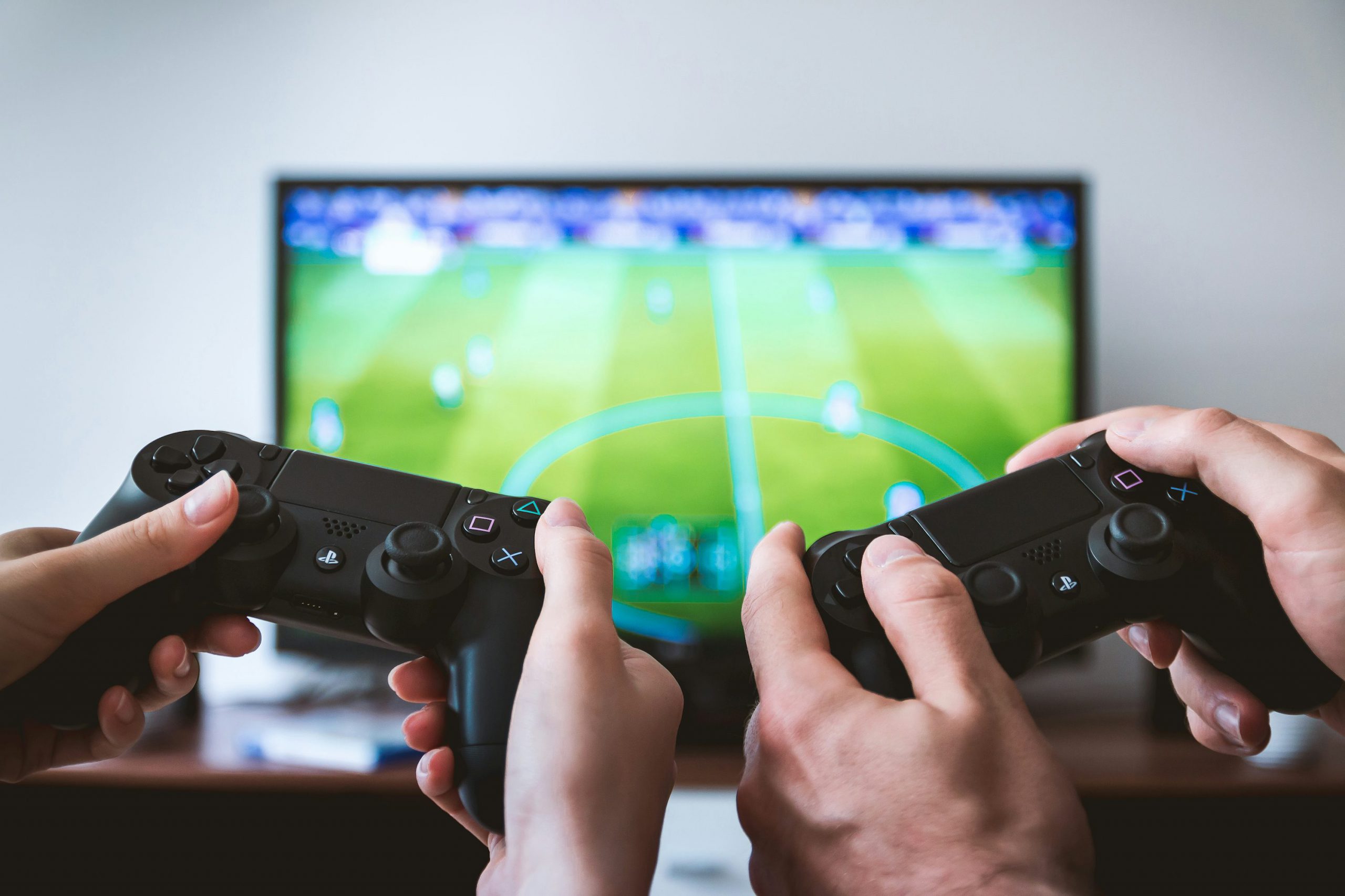 Duas pessoas jogando videogame multiplayer com controles de PlayStation em frente a uma TV